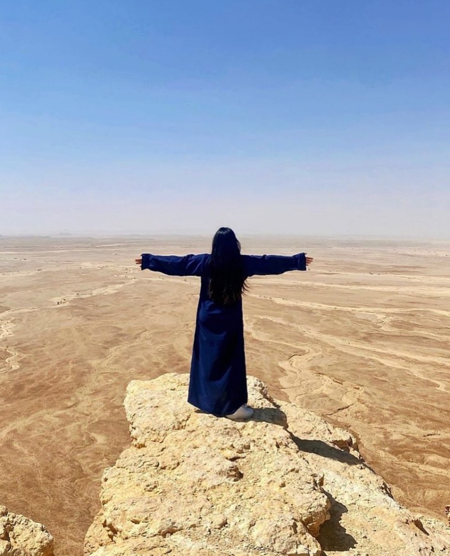 Jhayde standing with arms outstretched on a cliff at the Edge of the World in the desert