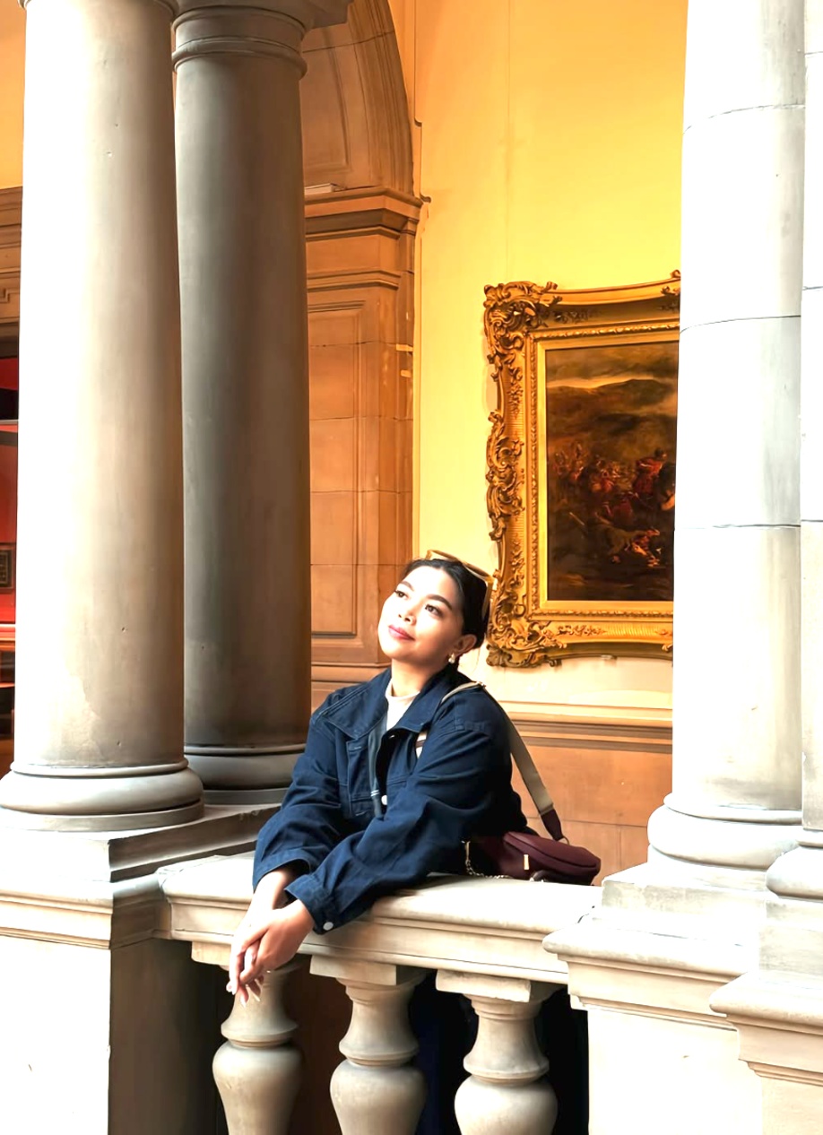 Jhayde sitting on a stone balustrade inside Kelvingrove Art Gallery in Glasgow, looking up